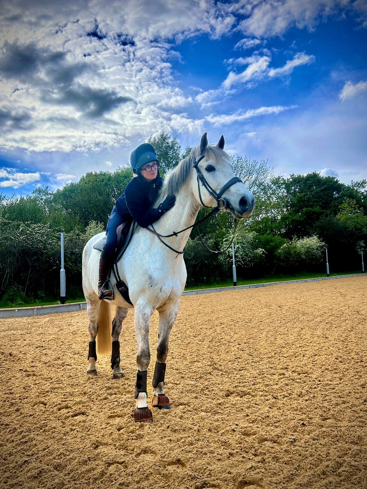 A rider leaning forward to pat a grey horse in the Tanglewood arena.